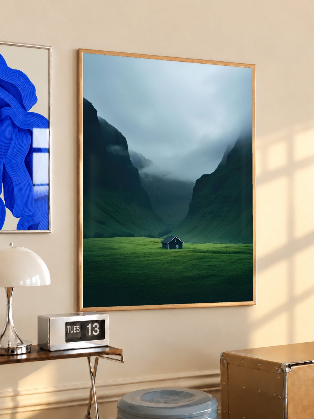 Wood-framed mountain valley print with misty blue peaks and a small green cabin