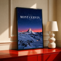 Snowy Mont Cervin beneath a starry navy sky and pink horizon; black framed print on a red cabinet