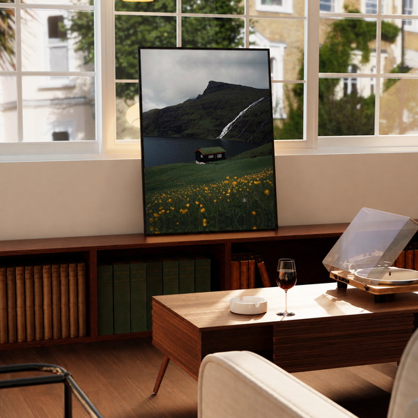 Moody Lake Cabin Wall Art in a black frame near a window and wooden table in a sunlit sitting room.