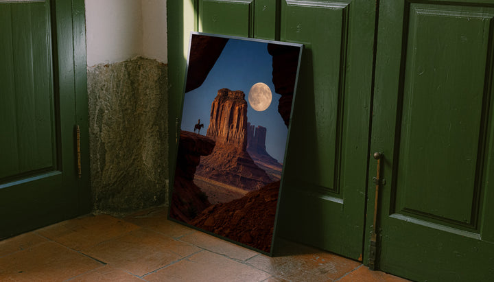 A horseback rider silhouetted beside a sandstone desert butte beneath a full moon leaning on the floor against dark green wall panelling