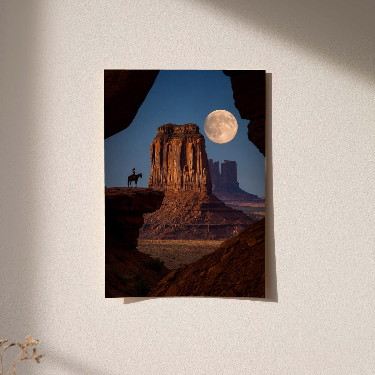 A horseback rider silhouetted beside a sandstone desert butte beneath a full moon displayed without a visible frame on a softly lit pale wall