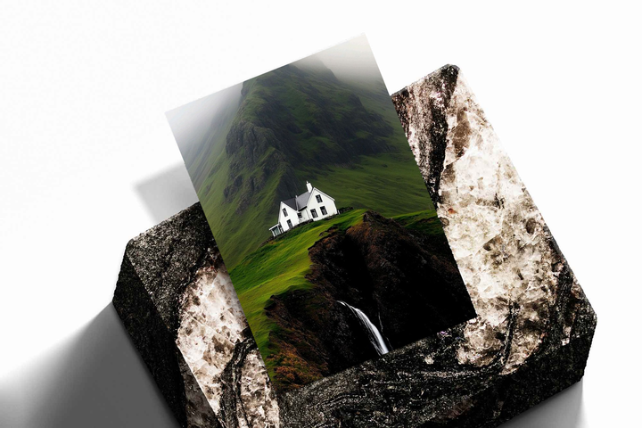 White cottage, misty mountain and waterfall as an unframed print propped against a pale wall on a rough stone