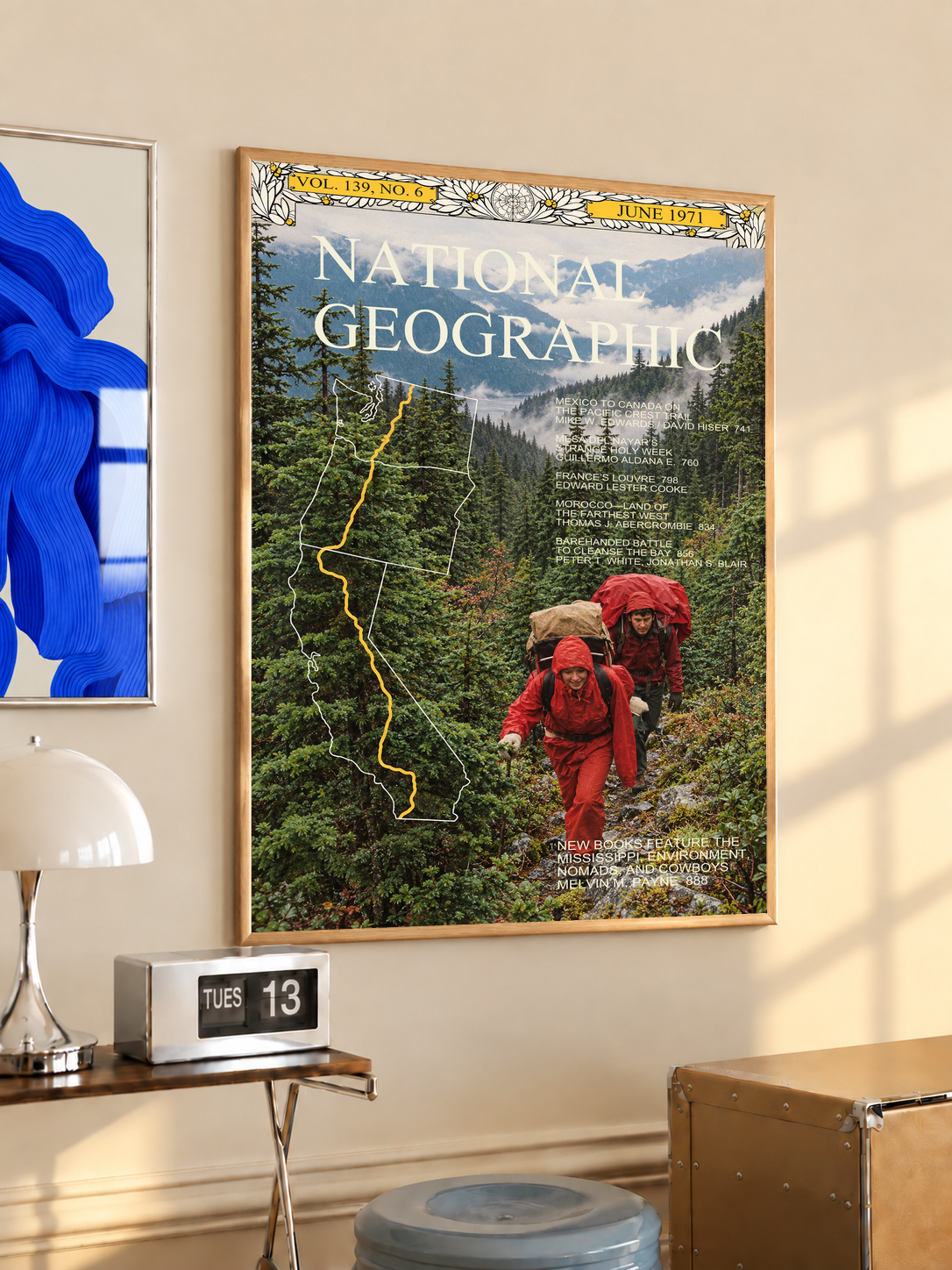 Red-jacketed hikers in a green forest with yellow route map and magazine-style heading; oak framed print in a desk setting