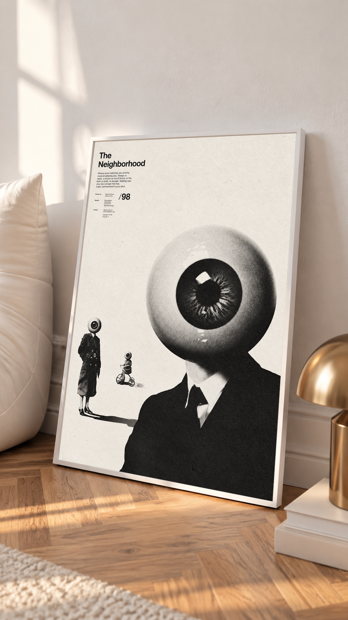 A suited eyeball-headed figure with smaller surreal figures on cream in a white frame on a sunlit floor beside a white cabinet