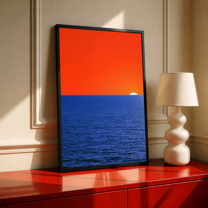 Framed coastal ocean sunset print with orange sky, blue water, and partial white sun