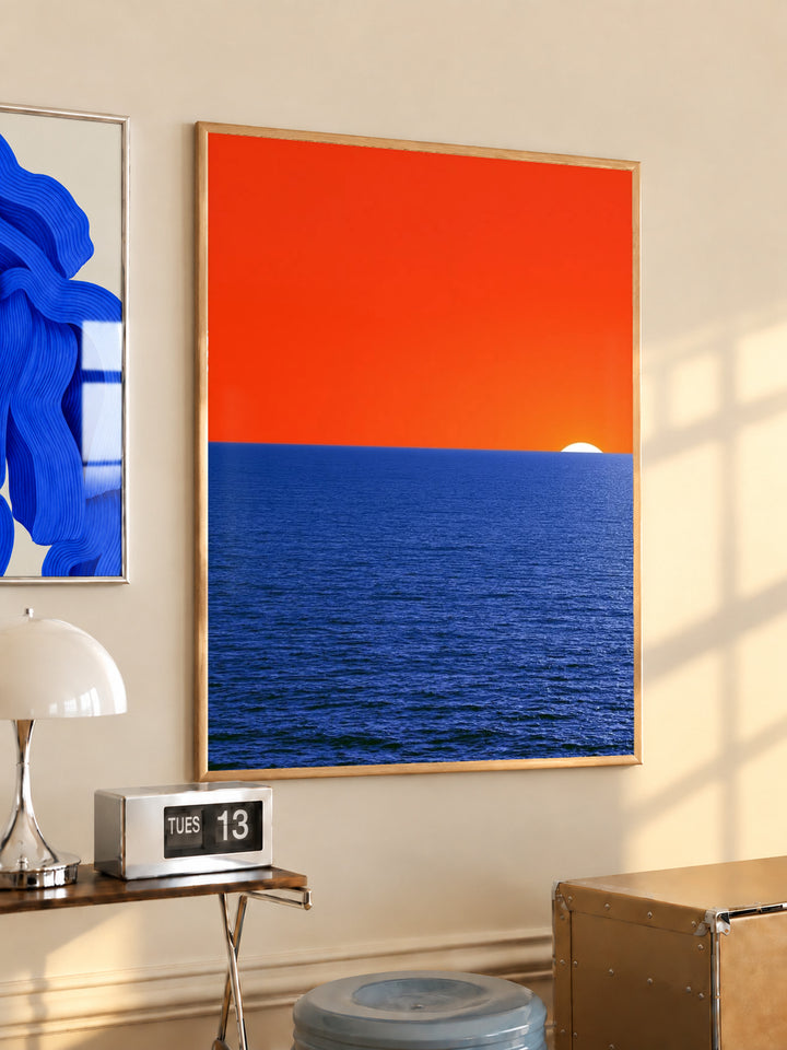 Coastal sunset wall art poster with orange sky, blue ocean, and a small white sun