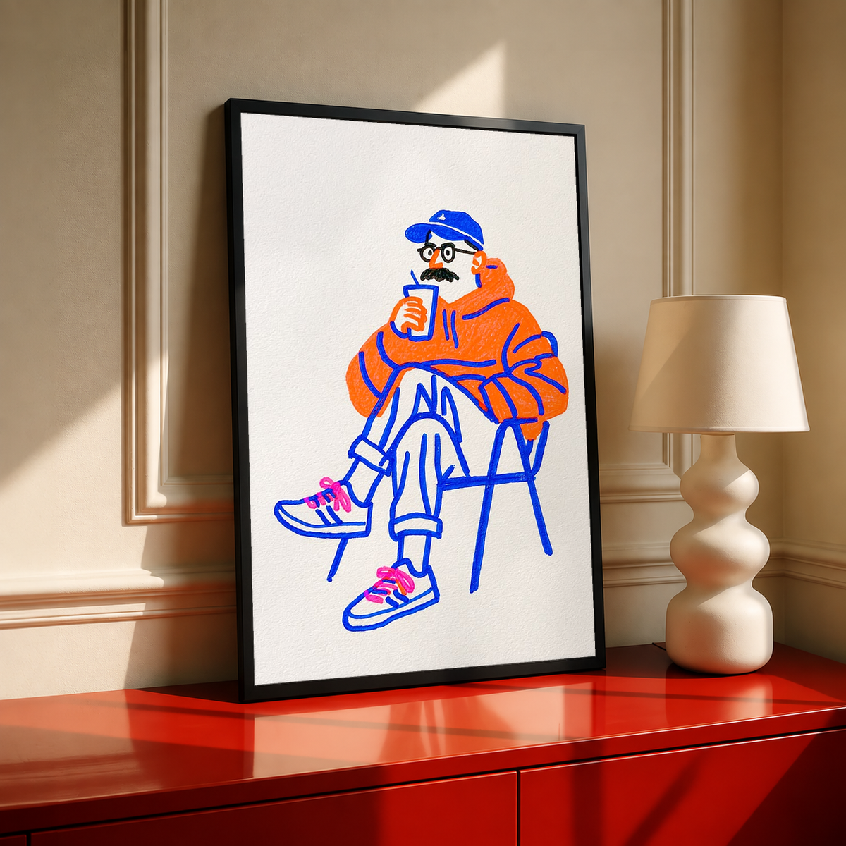 Black-framed coffee art print: seated orange character holding a cup, blue linework