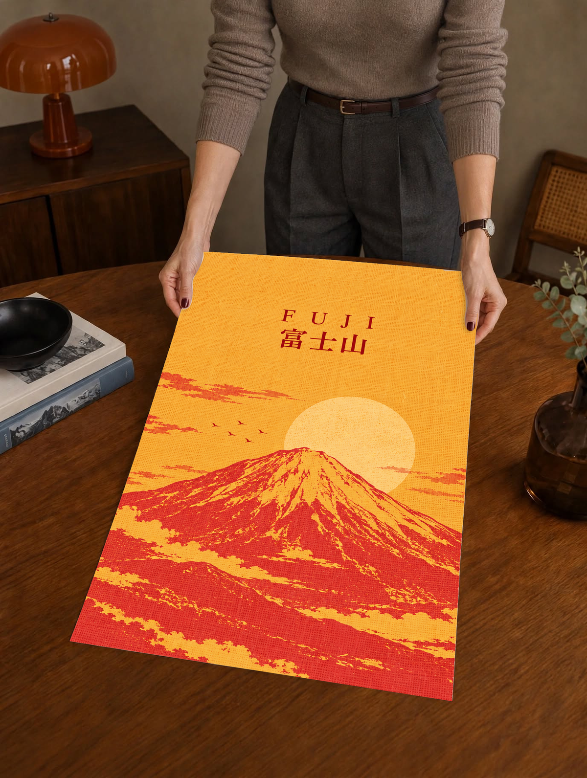 Mount Fuji sunrise poster held up, showing “FUJI” text, red mountain, and sun.
