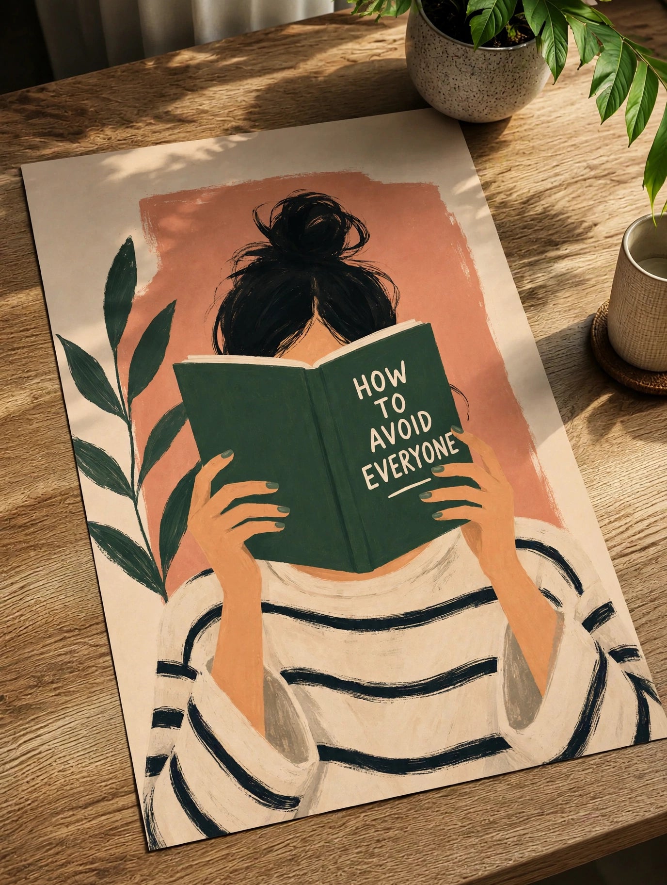 Framed wall art print on a wooden table, reading figure holding a green book with leaves