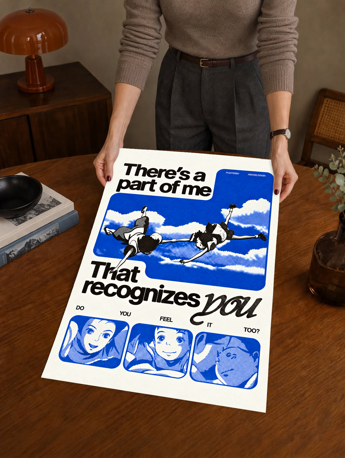 Two anime figures against blue sky with character portraits and a romantic recognition quote as a large unframed poster held above a wooden desk