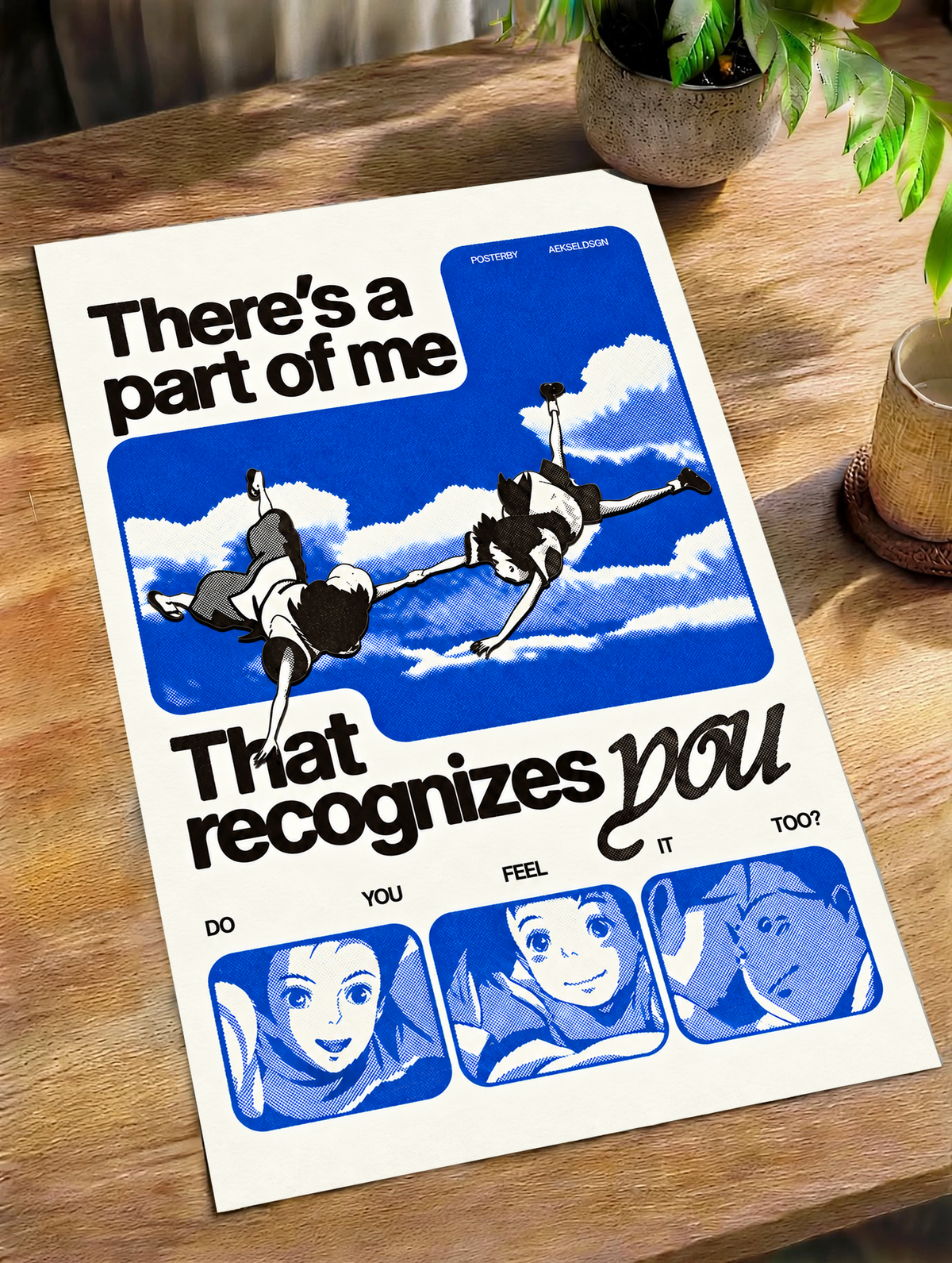 Two anime figures against blue sky with character portraits and a romantic recognition quote as an unframed poster lying on a wooden table beside a plant