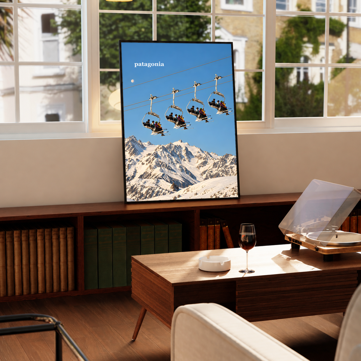 Skiers on chairlifts above snowy mountains beneath a muted blue sky; framed print beside a window