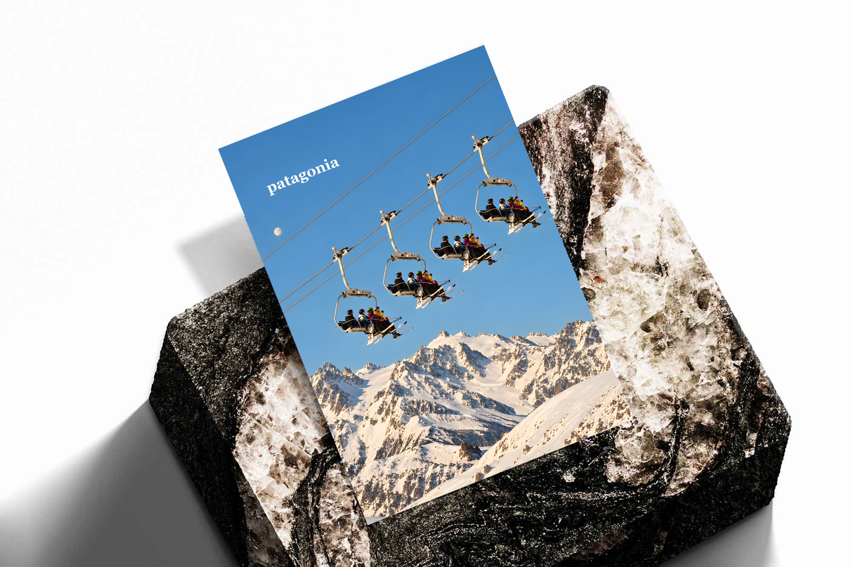 Skiers on chairlifts above snowy mountains beneath a muted blue sky; unframed print on a stone display