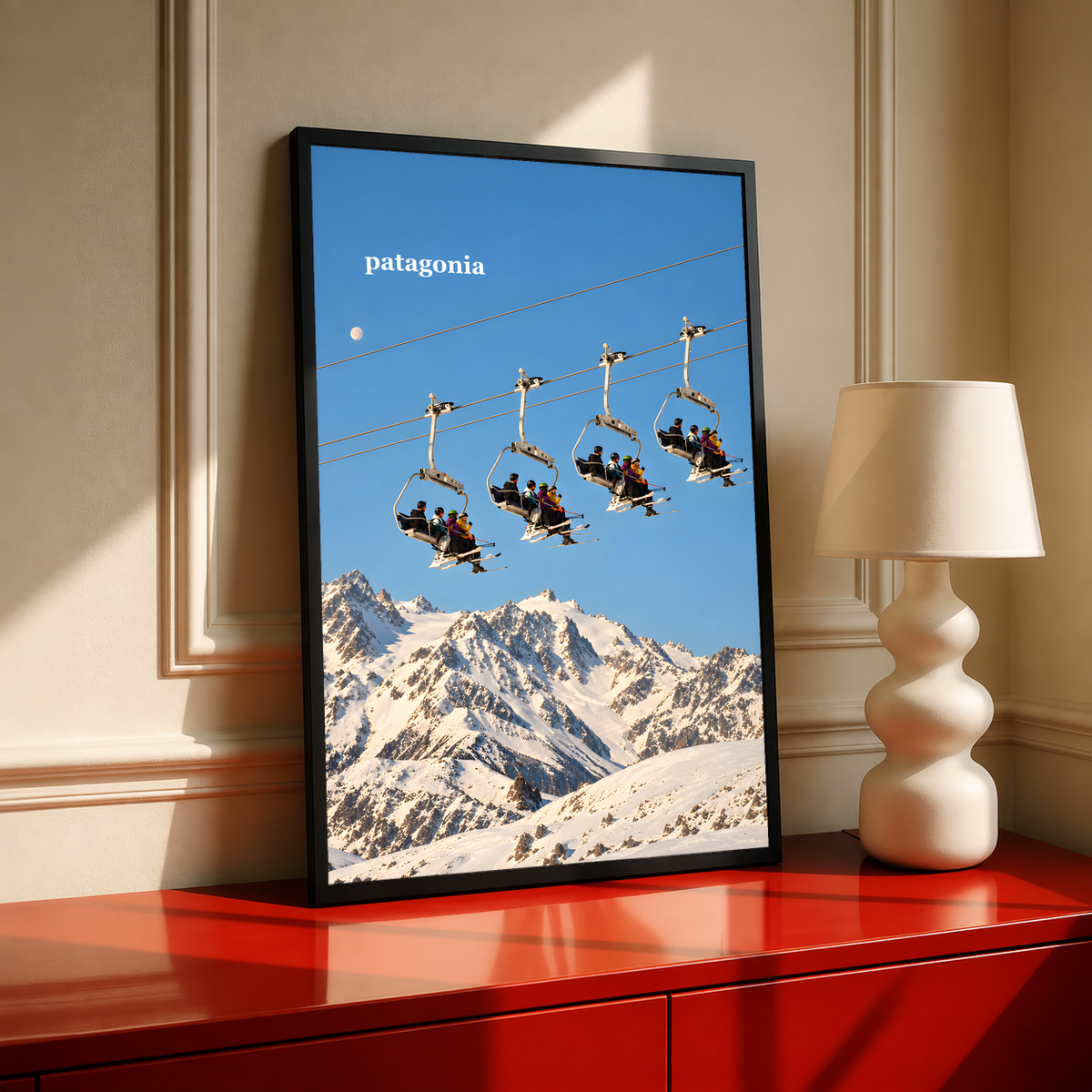Skiers on chairlifts above snowy mountains beneath a muted blue sky; black framed print on a red cabinet