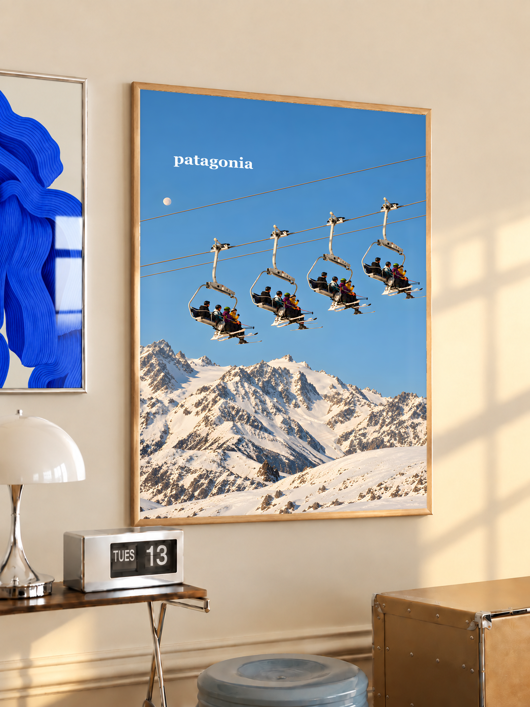 Skiers on chairlifts above snowy mountains beneath a muted blue sky; oak framed print in a desk setting