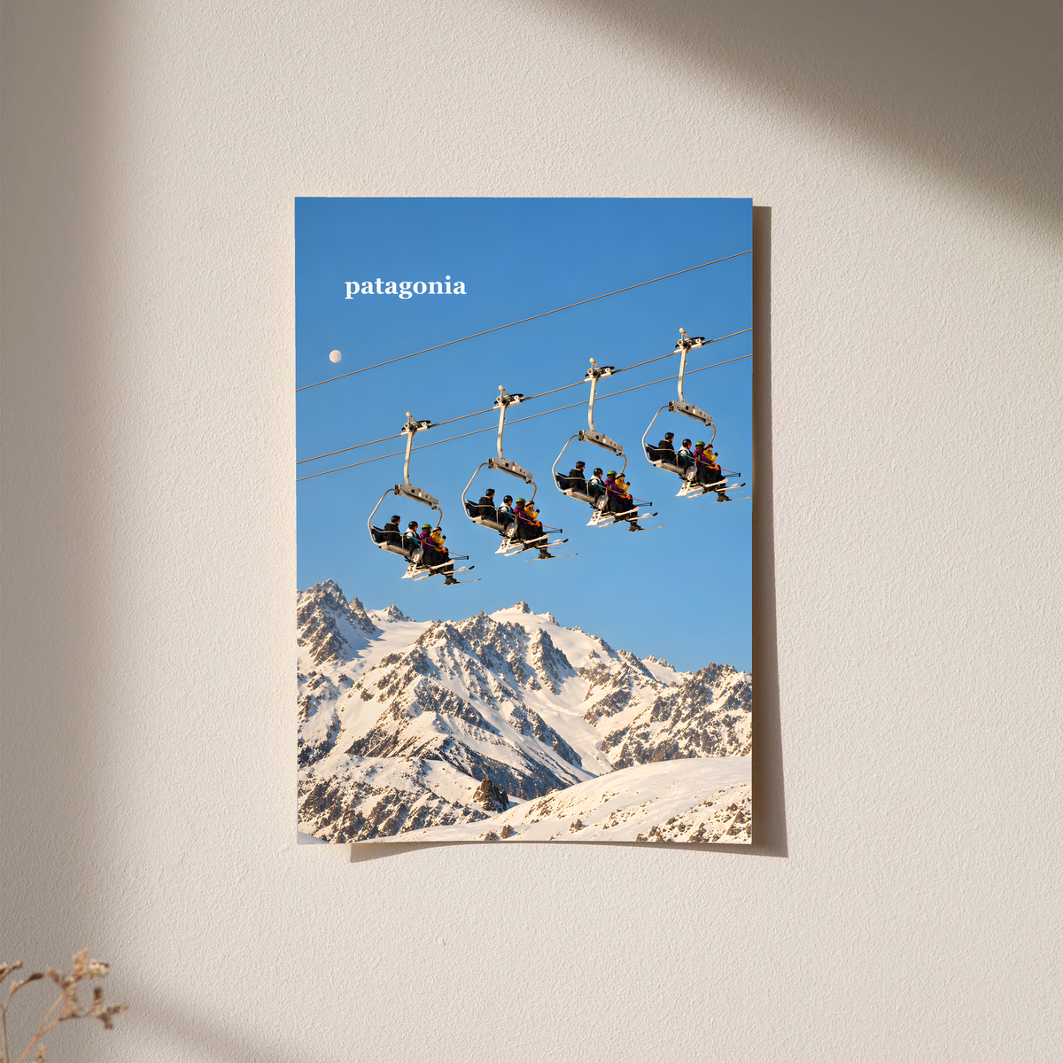 Skiers on chairlifts above snowy mountains beneath a muted blue sky; unframed print on a wall