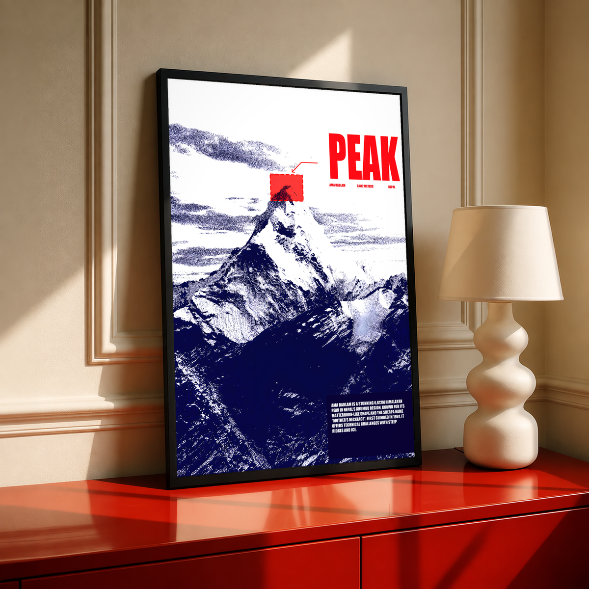 White and navy halftone Ama Dablam mountain with red PEAK lettering; black framed print on a red cabinet