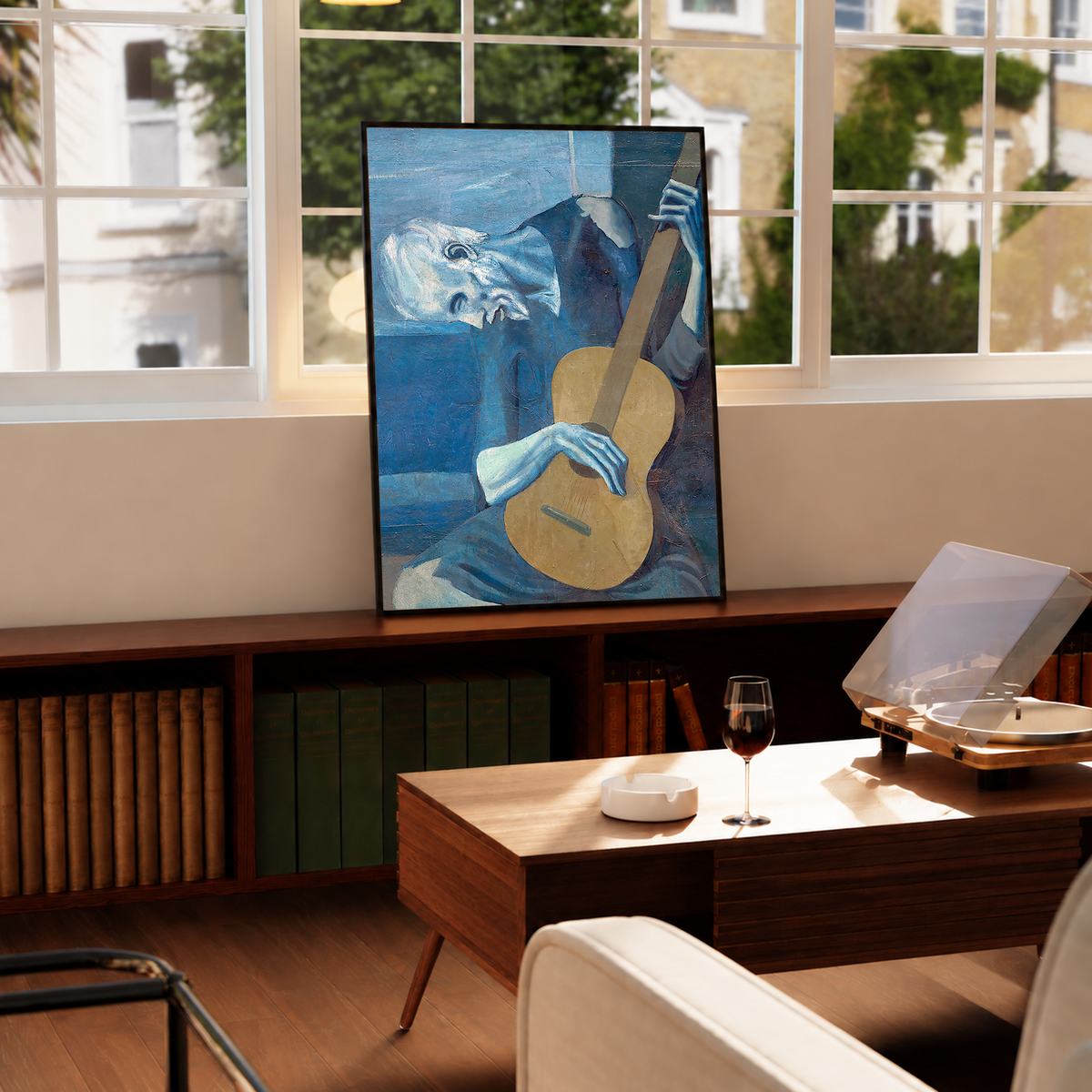 Picasso The Old Guitarist cropped portrait with a bowed blue figure and ochre guitar in a black frame on a cabinet beside a window and record player