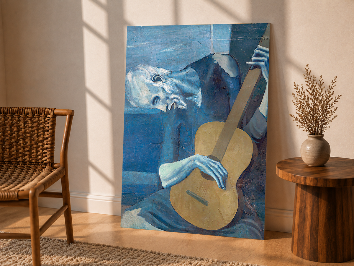 Picasso The Old Guitarist cropped portrait with a bowed blue figure and ochre guitar as an unframed display leaning beside a wicker chair and side table