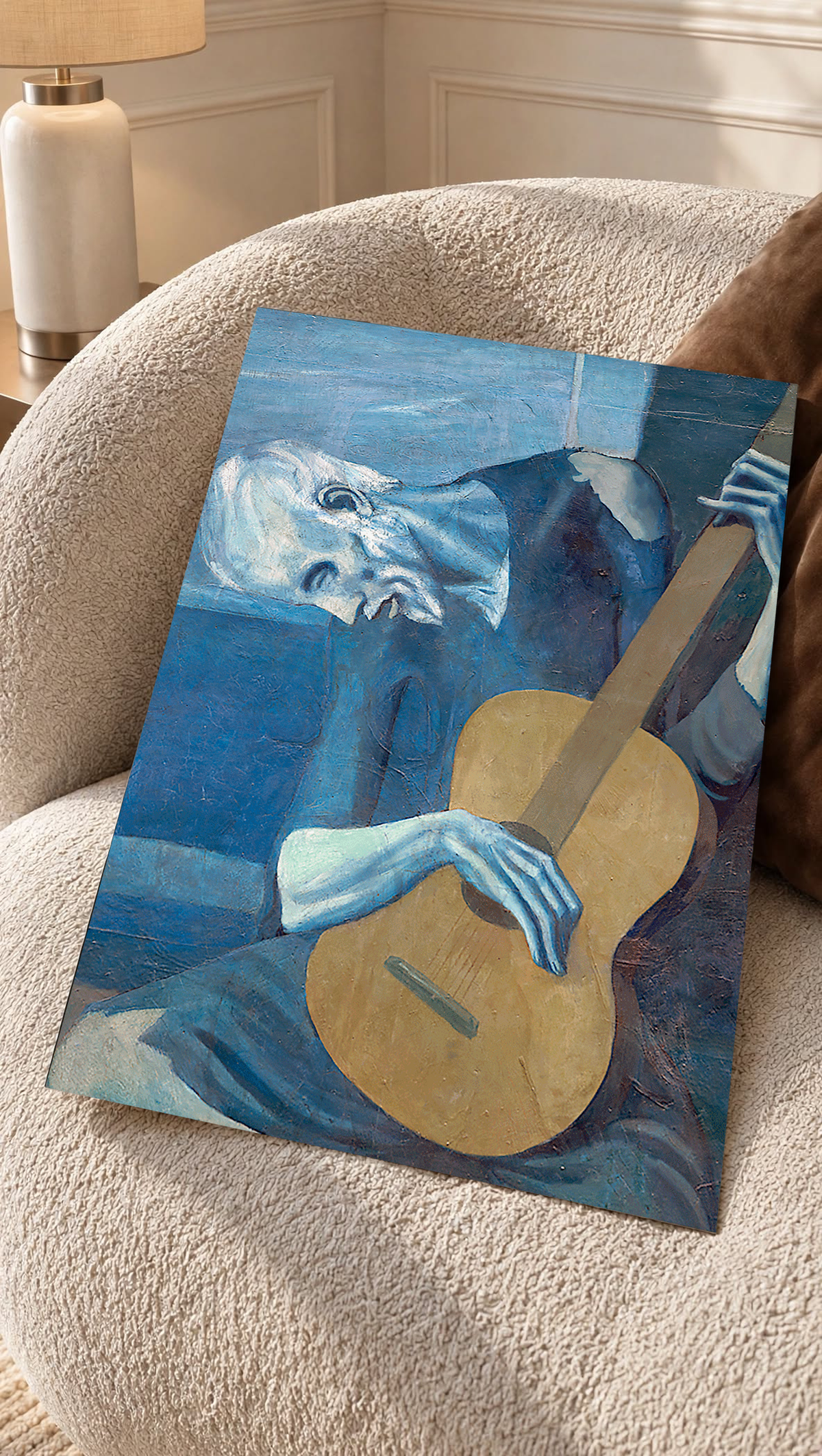 Picasso The Old Guitarist cropped portrait with a bowed blue figure and ochre guitar as an unframed print resting on a boucle chair