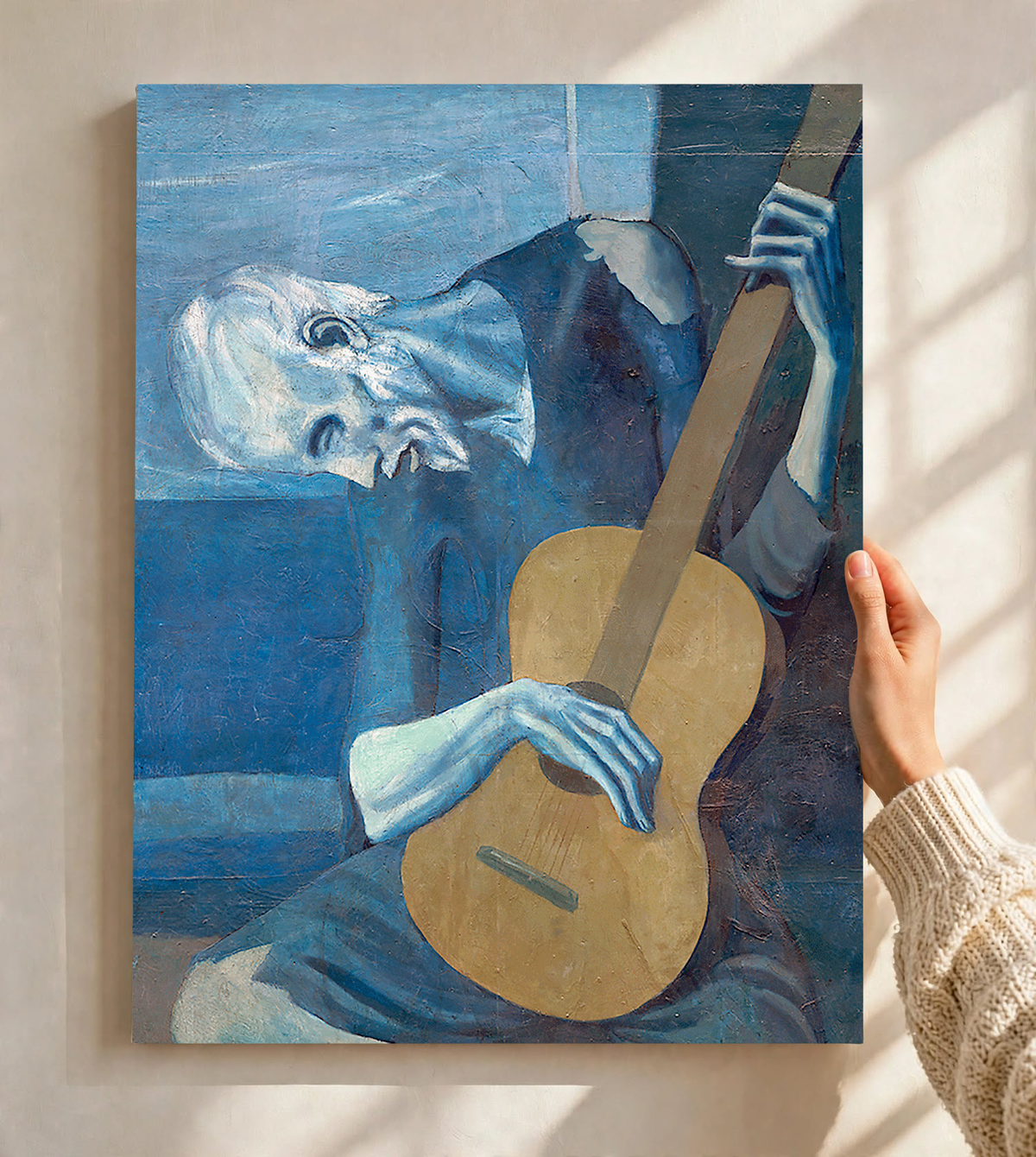 Picasso The Old Guitarist cropped portrait with a bowed blue figure and ochre guitar as an unframed print held against a pale wall in a close view