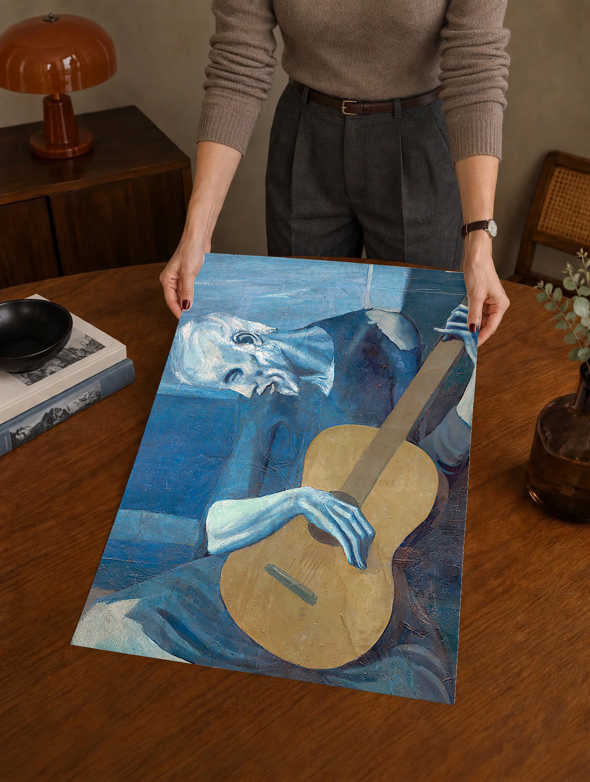 Picasso The Old Guitarist cropped portrait with a bowed blue figure and ochre guitar as an unframed print held over a wooden table beside a record player