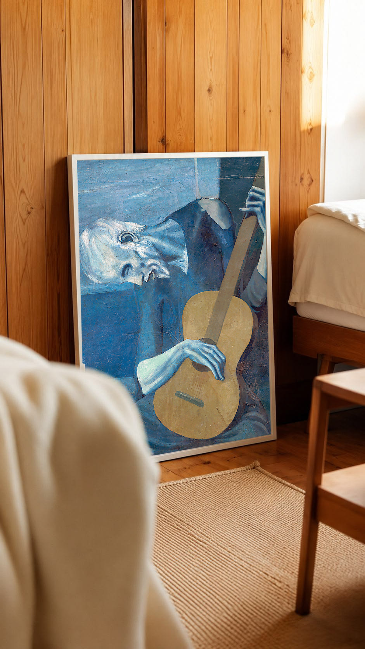 Picasso The Old Guitarist cropped portrait with a bowed blue figure and ochre guitar in a white frame in a wood-panelled bedroom