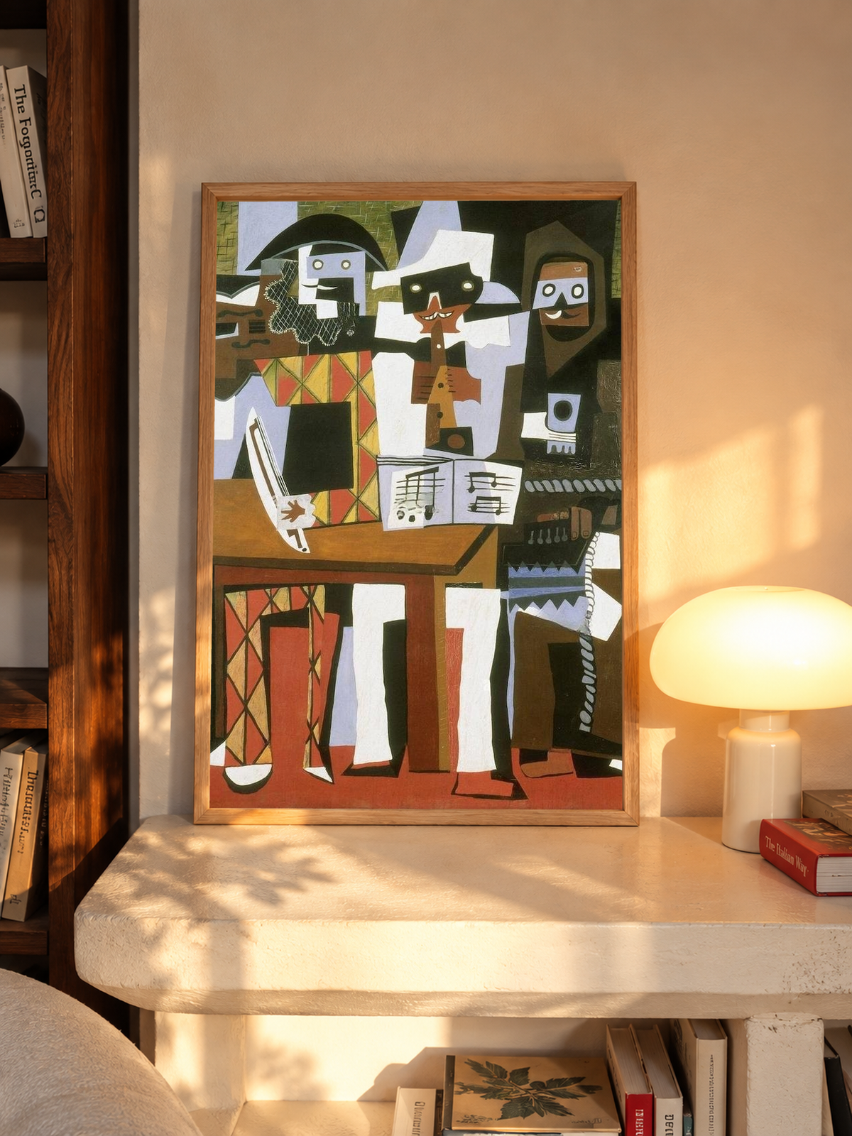 Picasso Three Musicians with angular masked figures, red diamonds and an accordion in an oak frame on a sunlit console beside books and a cream lamp