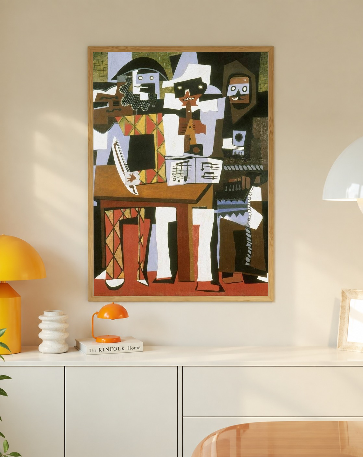 Picasso Three Musicians with angular masked figures, red diamonds and an accordion in an oak frame on a wall above a white cabinet beside a yellow lamp