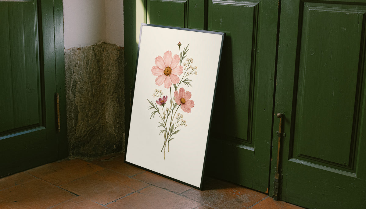 Pink cosmos flowers with yellow centres and fine white botanical sprigs as an unframed print leaning against a green panelled door