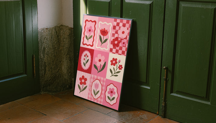 A pink and red patchwork grid of tulips, daisies, scalloped frames and checkerboard squares leaning on the floor against dark green wall panelling