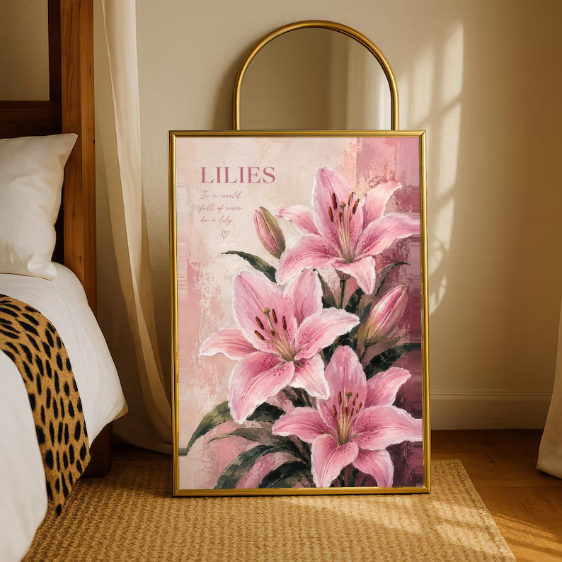 Pink lilies and buds with dark green leaves beneath a LILIES heading on a soft blush ground in a gold-tone styling frame leaning beside a bedroom mirror