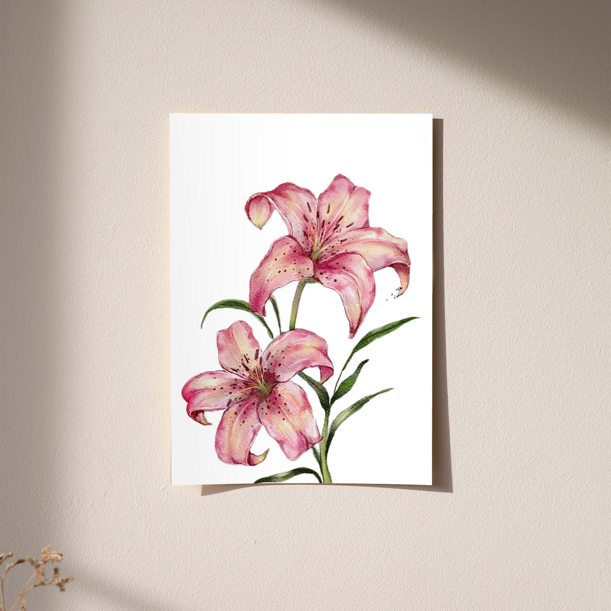 Two pink lilies with speckled petals and green leaves against white as an unframed hanging paper print against a plaster wall
