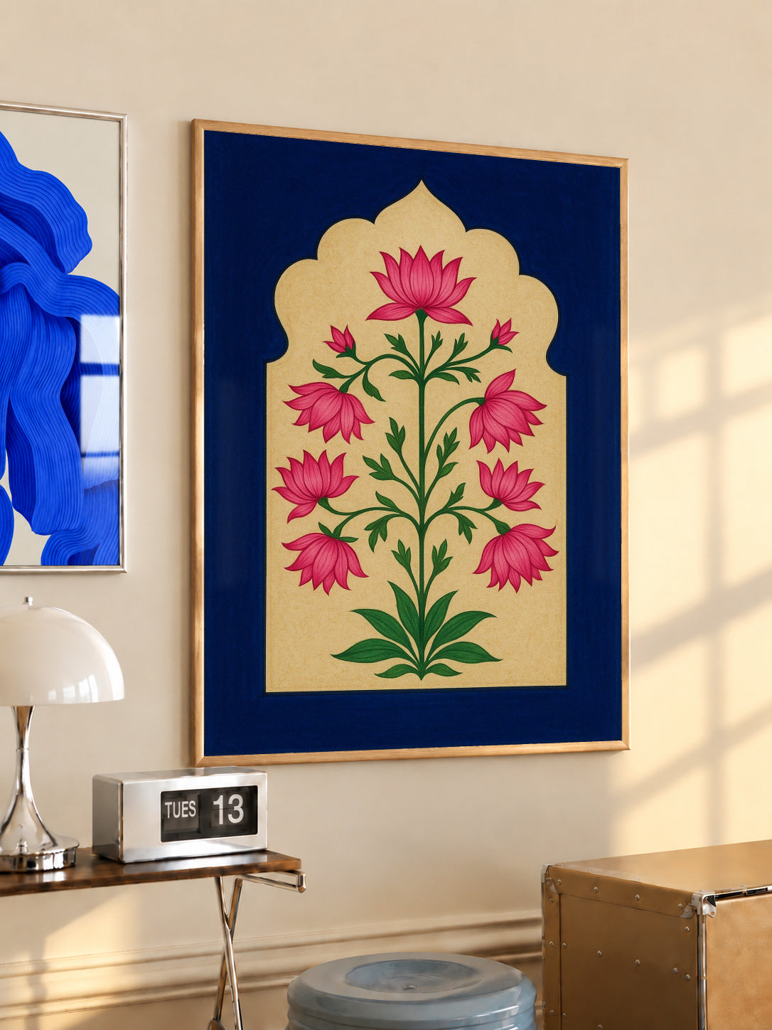 Pink lotus-like flowers and green stems within a scalloped gold arch on navy blue in a light wood frame on a sunlit office wall beside a desk
