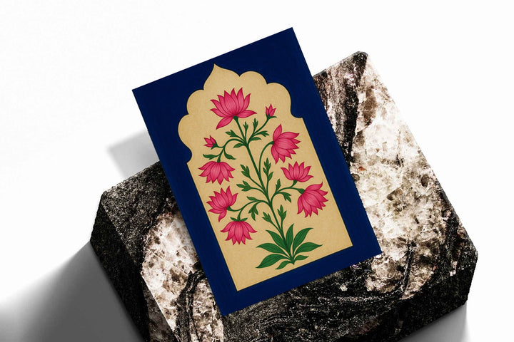 Pink lotus-like flowers and green stems within a scalloped gold arch on navy blue as an unframed print resting at an angle on a dark stone display