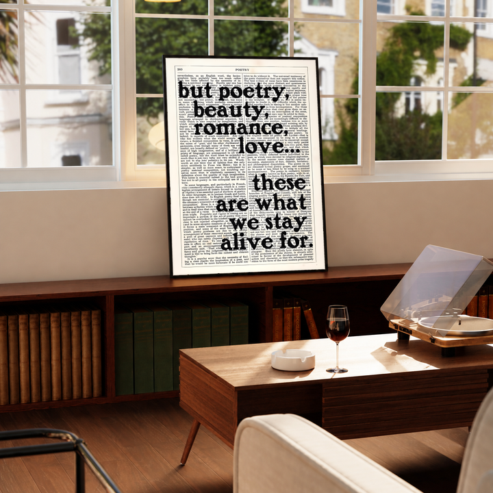 Poetry beauty romance love quote in black serif lettering over a cream two-column book page, styled in a black frame above a wood console with books and a record player
