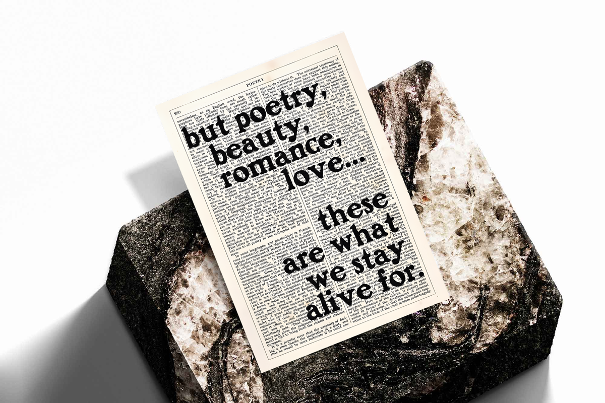 Poetry beauty romance love quote in black serif lettering over a cream two-column book page, shown as an unframed print tilted on a dark stone display against a light background