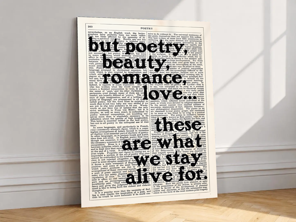Poetry beauty romance love quote in black serif lettering over a cream two-column book page, shown unframed on a white wall above parquet flooring with a diagonal sun shadow
