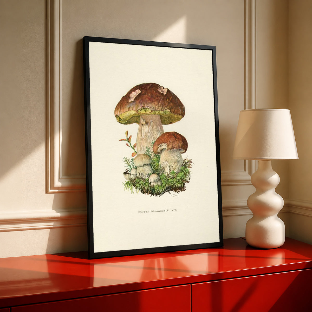Brown porcini mushrooms with moss and a printed Steinpilz Boletus edulis caption in a black frame on a red cabinet beside a cream lamp