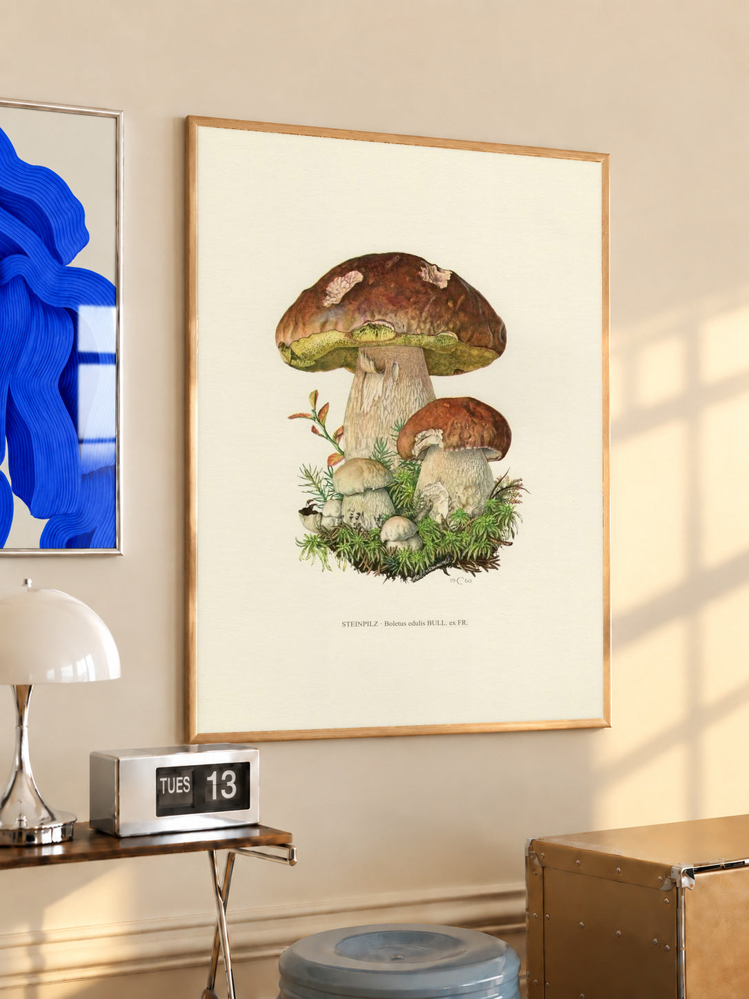 Brown porcini mushrooms with moss and a printed Steinpilz Boletus edulis caption in an oak frame above a console beside a blue print and calendar