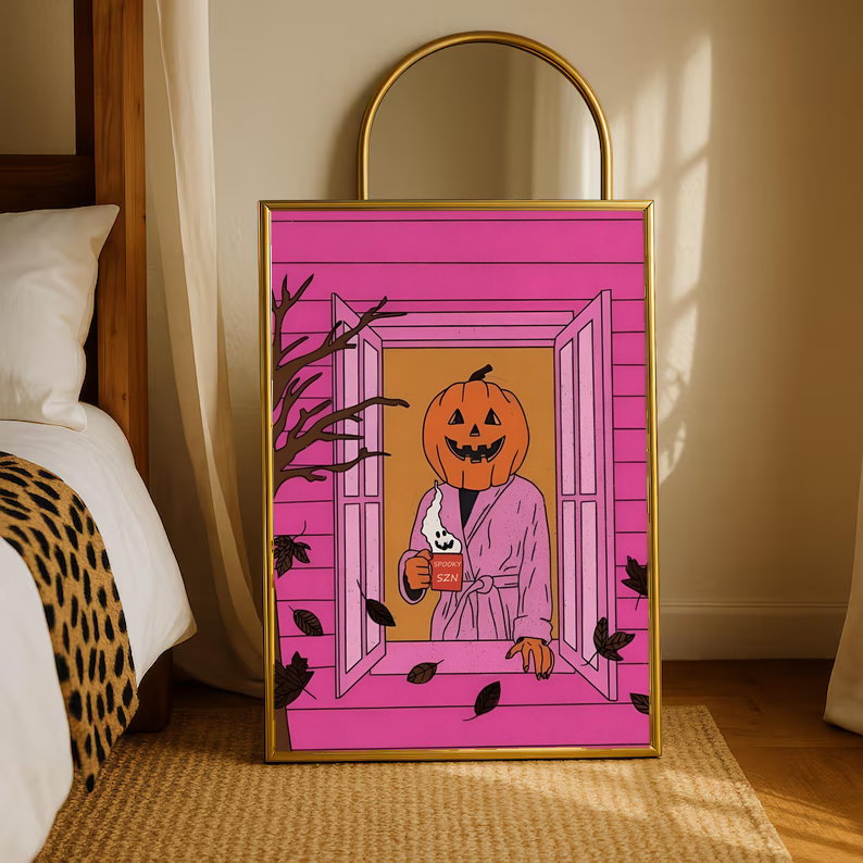 Gold-framed Halloween poster standing on rug, jack-o'-lantern holding a mug in pink doorway