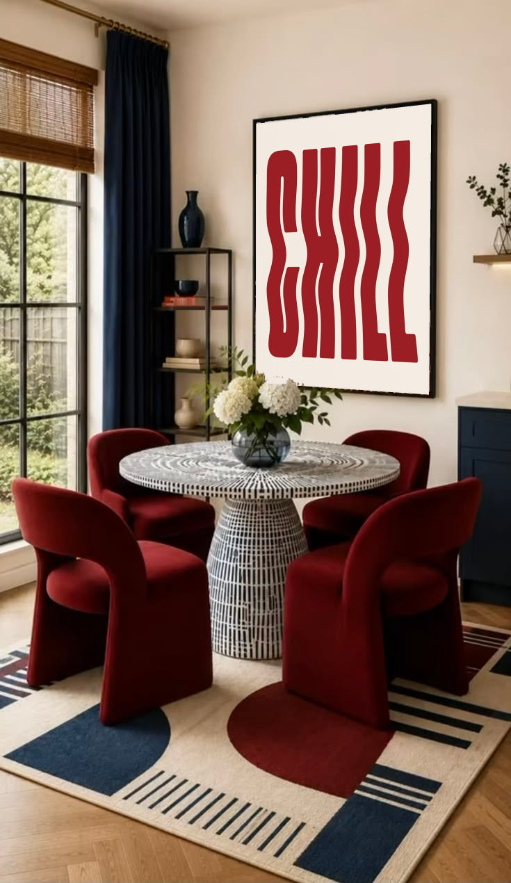 The word CHILL in tall wavy red lettering on a cream background in a black frame on the wall of a dining nook with red chairs