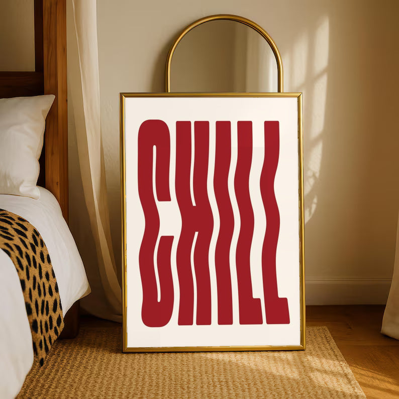 The word CHILL in tall wavy red lettering on a cream background in a gold-tone styling frame leaning beside a bedroom mirror