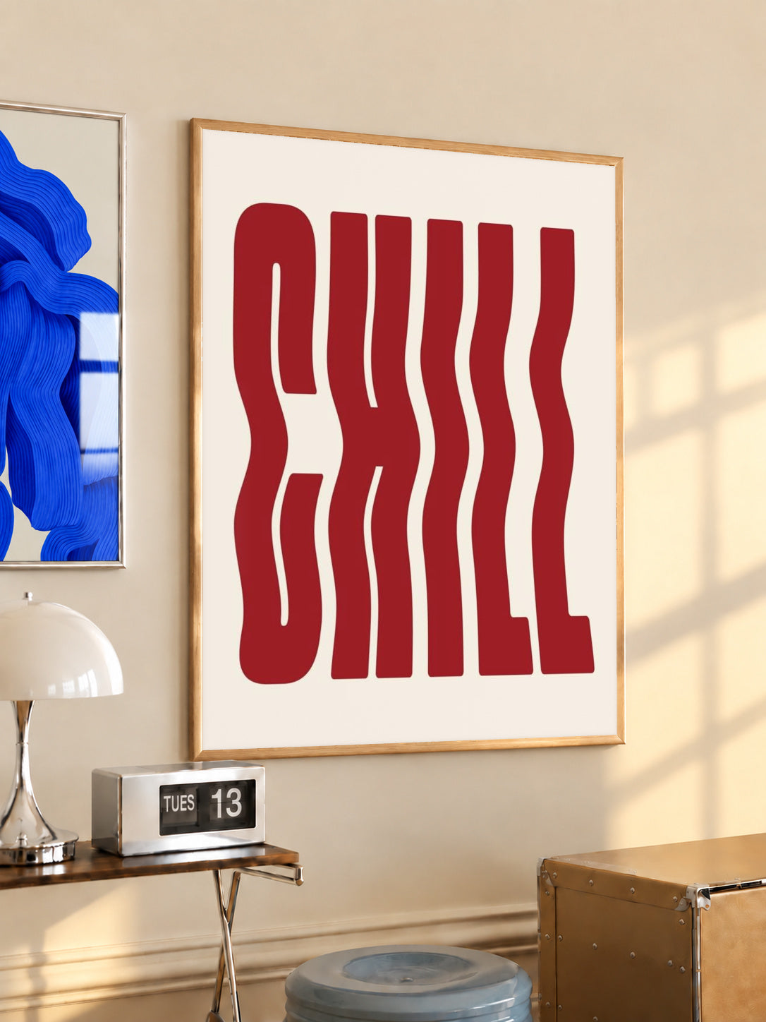The word CHILL in tall wavy red lettering on a cream background in a light wood frame on a sunlit office wall beside a desk