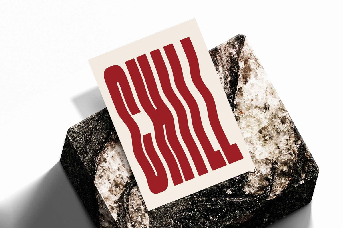 The word CHILL in tall wavy red lettering on a cream background as an unframed print resting at an angle on a dark stone display