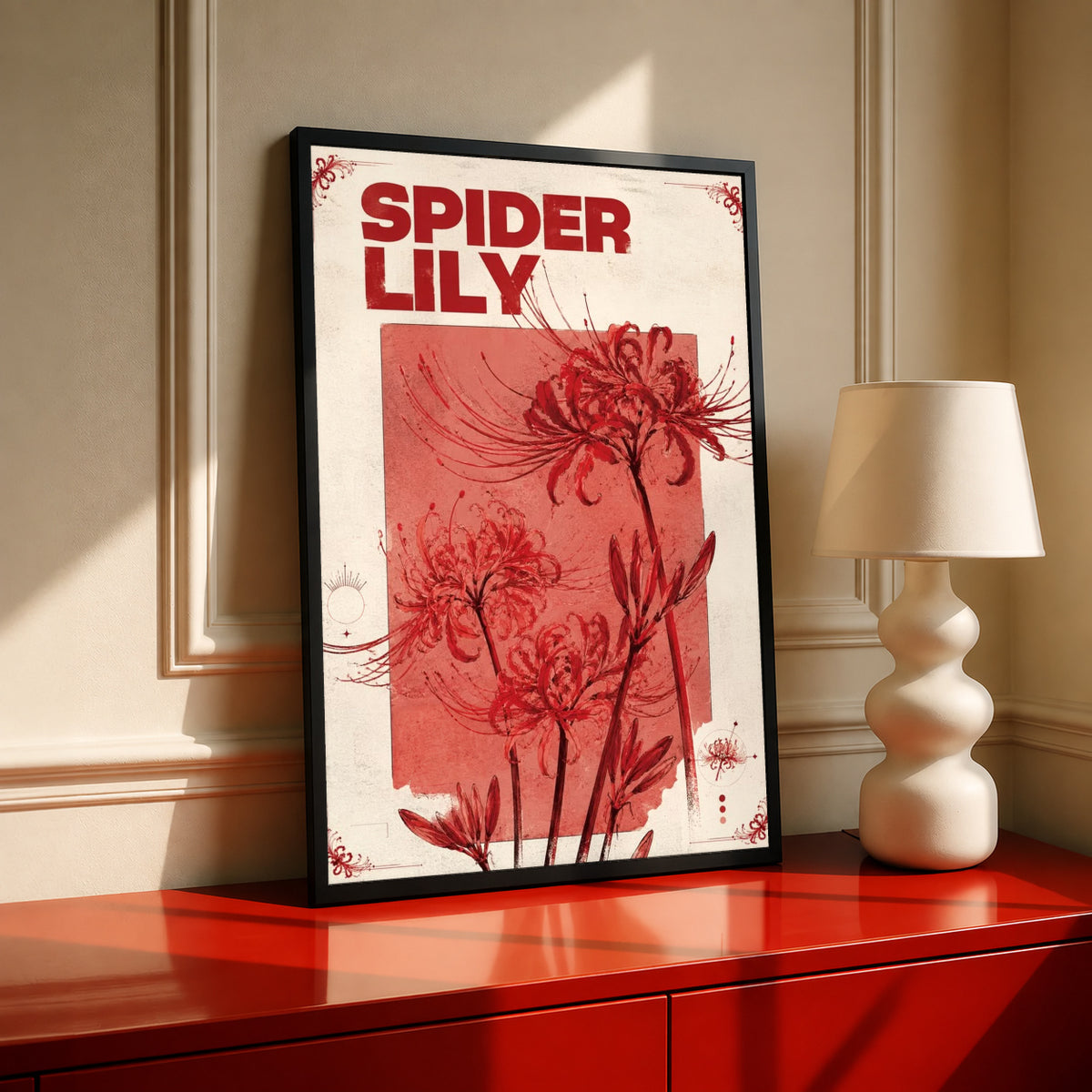 Red spider lily flowers and the words SPIDER LILY in a vintage cream and red botanical design in a black frame on a red console beside a sculptural cream lamp