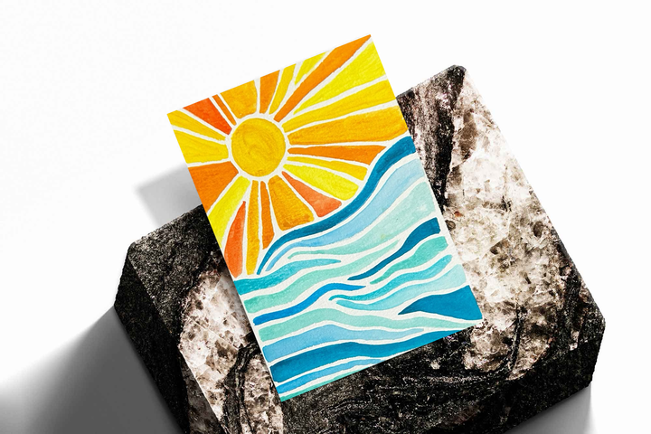 Sun rays over ocean waves as an unframed print propped against a pale wall on a rough stone