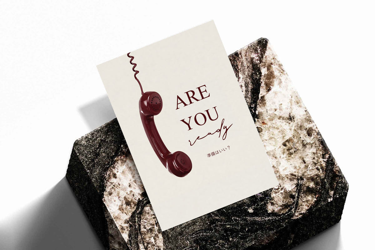 Telephone typography poster with burgundy 'ARE YOU' on cream, placed on stone surface