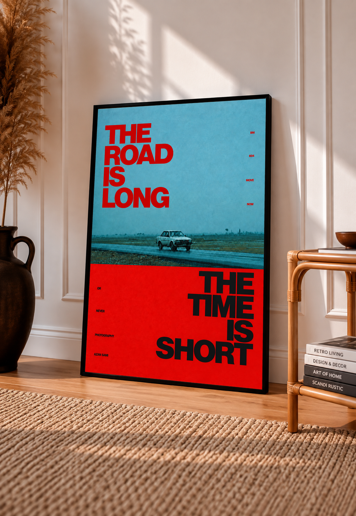 A small vintage car between blue and red blocks with bold road and time lettering in a black frame leaning on a sunlit floor beside a rattan chair