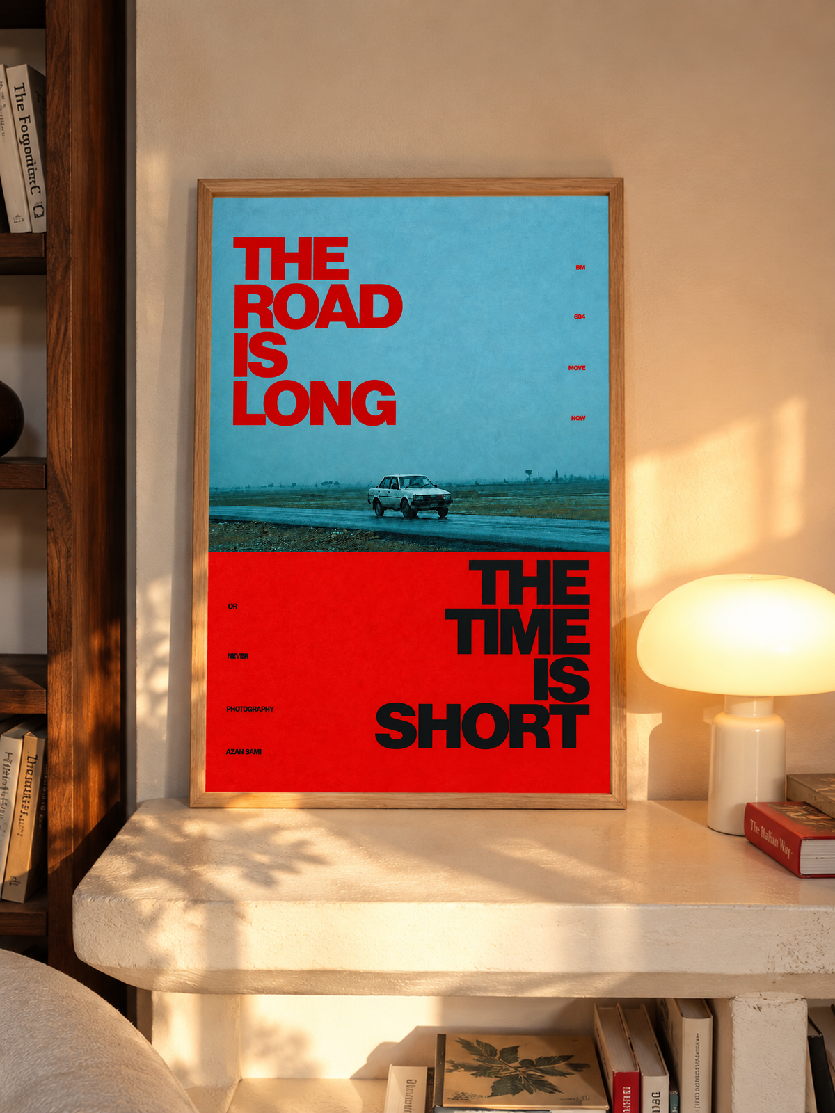 A small vintage car between blue and red blocks with bold road and time lettering in an oak frame above a pale wooden sideboard beside a glowing lamp